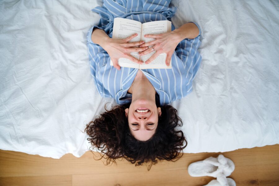 woman lying on her back across a bed with a book