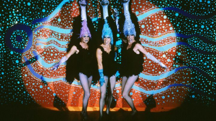 Priscilla takes the stage in blue hair, black mini dress and fishnet stockings along with two others