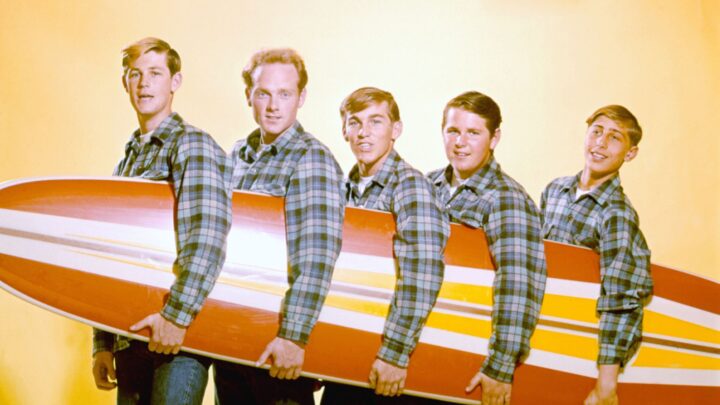 Vintage photo of the Beach Boys posing in plaid shirts holding a surfboard