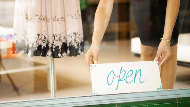 women putting an open sign in shop window, thinkstock