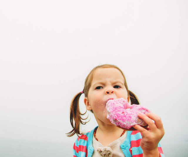 Little girl eating a pink iced donut. Too much sugar.