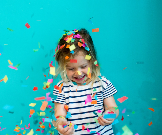 Small child throwing confetti against turquoise wall