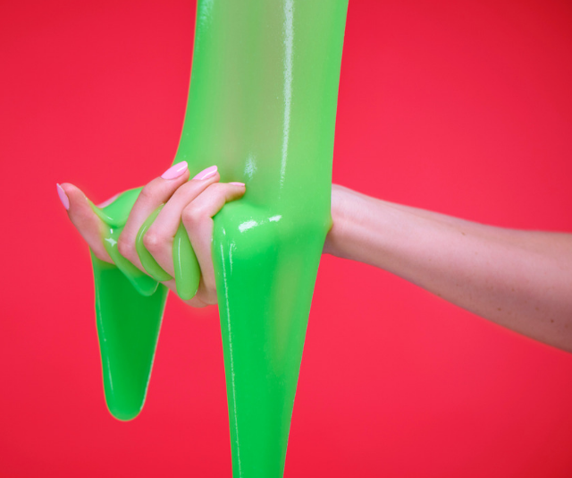 Hand held out against red background as green slime is poured onto it.