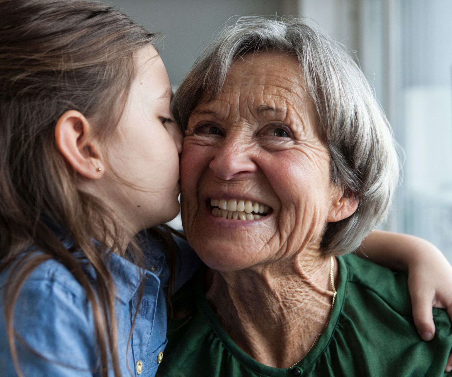 girl kissing her grandmother on the cheek and hugging
